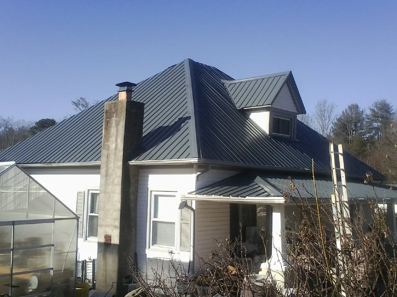 Dark blue standing seam metal roof on a white farmhouse with dormer — Slate & Tile Roof Repair by Roofing Brothers in Avery Island