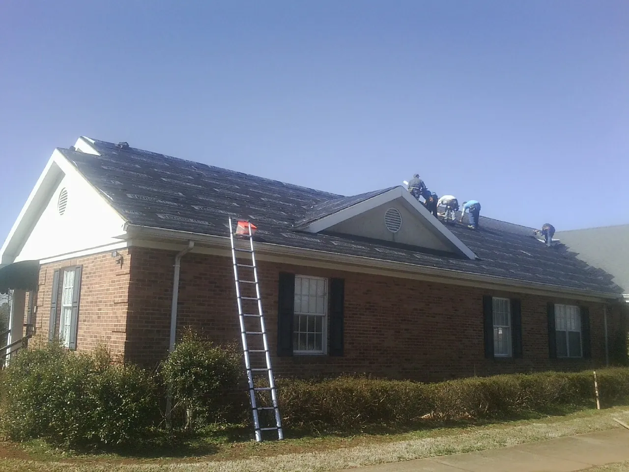 Crew tearing shingles off a brick ranch roof with a ladder set — Emergency Roof Repair work by our crew in Avery Island