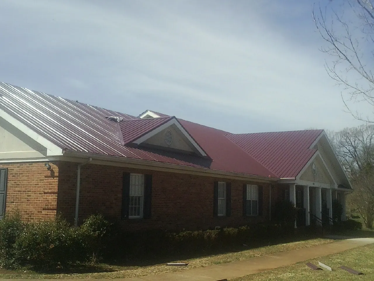 Red metal roof with gabled entries on a long brick building, from a Hail Damage Roof Repair job in Avery Island