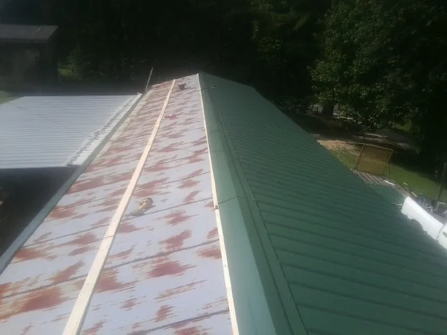Old rusted panels beside newly installed green metal roofing — Wind Damage Roof Repair by Roofing Brothers in Avery Island