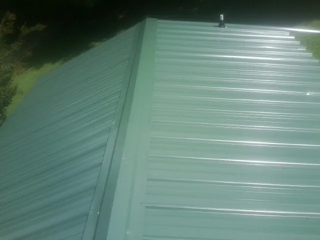 New green metal panels meeting at the ridge of a roof — Flat Roof Repair work by our crew in Avery Island