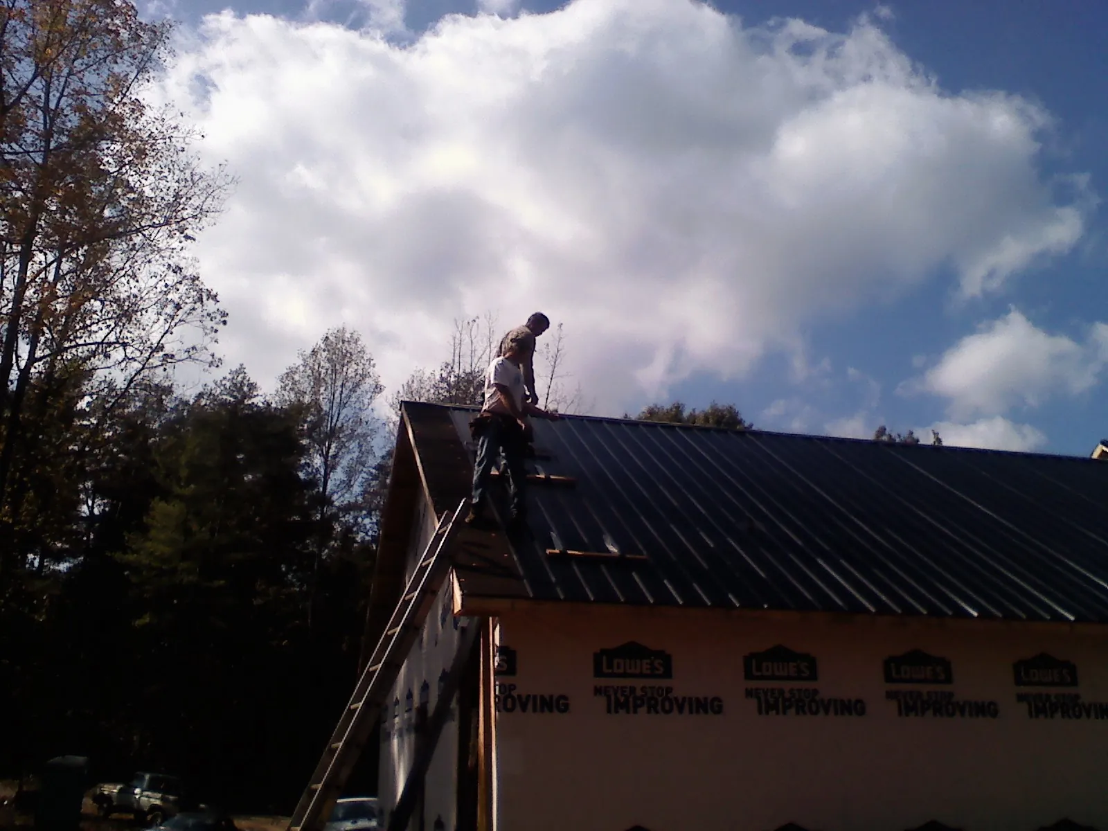 Roofer fastening dark metal panels high against a cloudy sky, from a Roof Inspection job in Avery Island