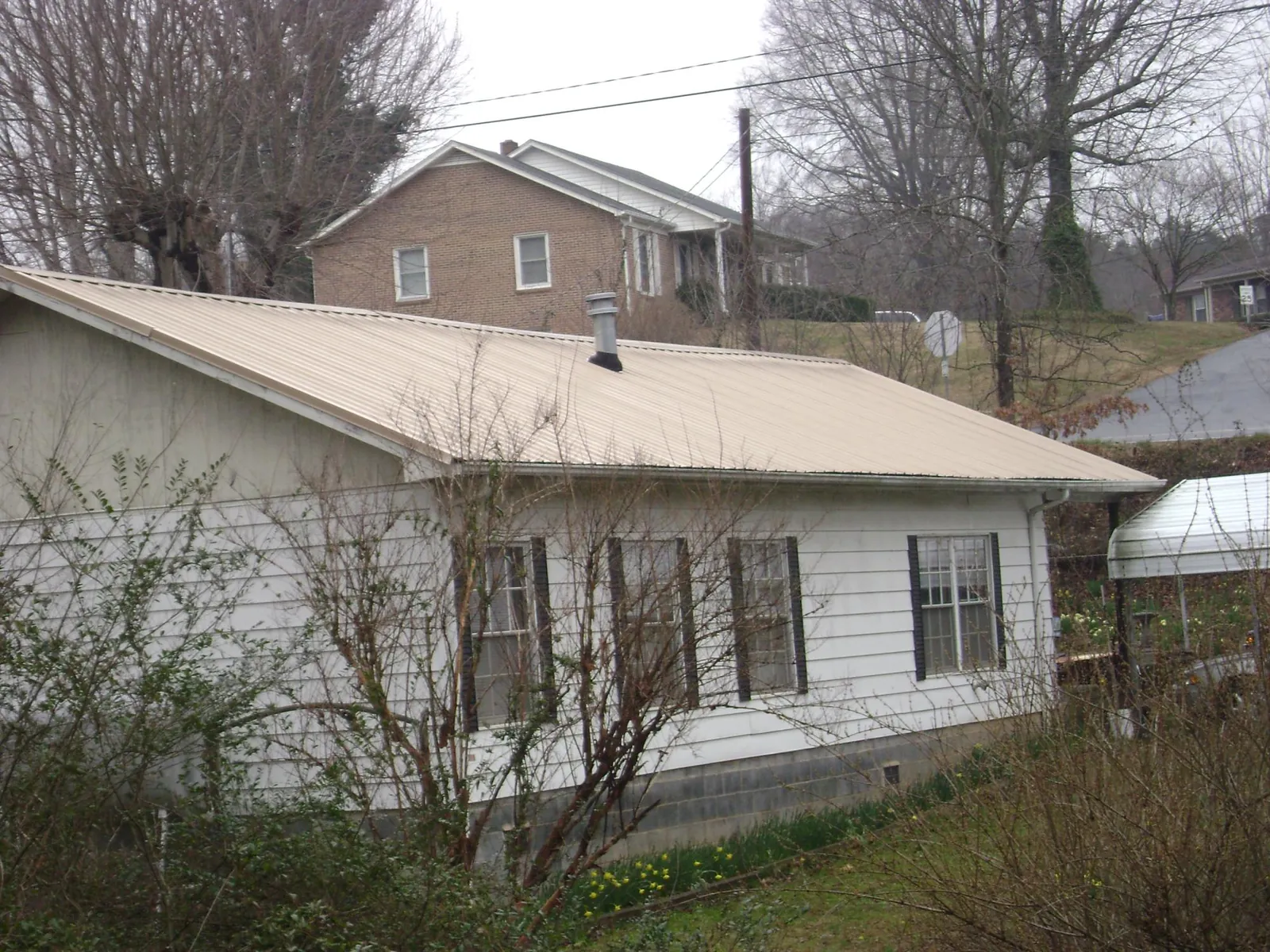 Tan metal roof on a white sided house set into a hillside — Commercial Roofing by Roofing Brothers in Avery Island